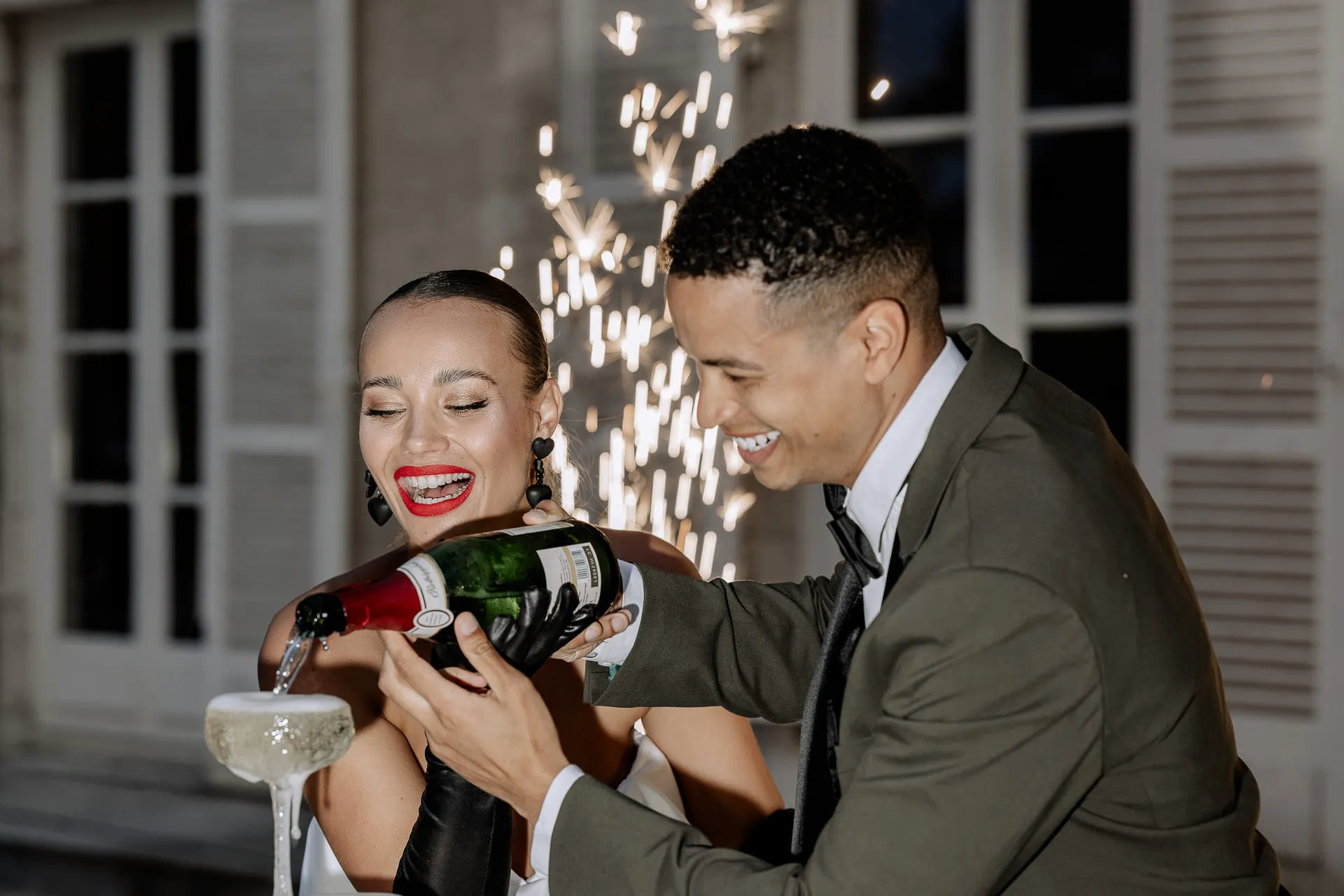 Bridal couple pouring champagne together with fireworks in background at Chateau de Varennes